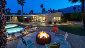 A modern outdoor patio with a fire pit, lounge chairs, and a pool.