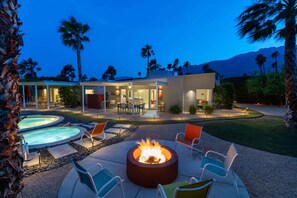 A modern outdoor patio with a fire pit, lounge chairs, and a pool.