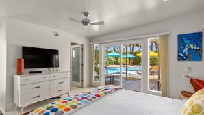 A bedroom with a bed, a TV on a dresser, and a view of an outdoor pool area.