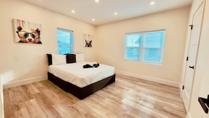 Un dormitorio con cama, suelo de madera y dos ventanas con persianas.