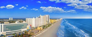 A coastal hotel with multiple high-rise buildings, a beach, and a clear blue sky. - Beachline Breeze on the Strip (Daytona Beach)