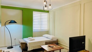 Una habitación pequeña y bien iluminada con cama, mesita de noche, lámpara y televisor.