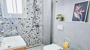 Un baño moderno con un lavamanos blanco, una ducha con puerta transparente, un inodoro y un soporte verde para cepillo de limpieza.