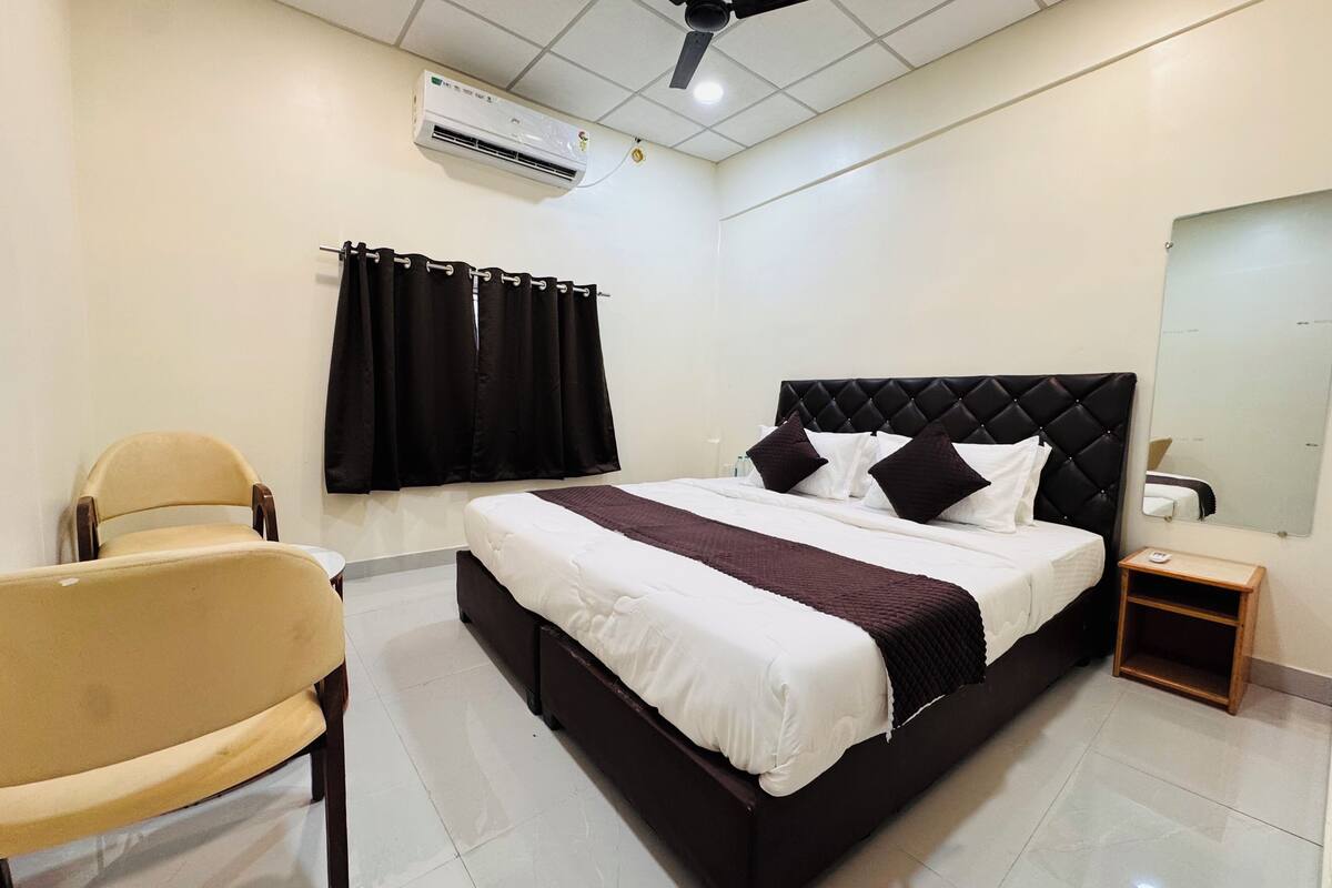 Une chambre d’hôtel équipée d’un lit, d’une chaise, d’une table de chevet, d’un climatiseur et d’un ventilateur de plafond.