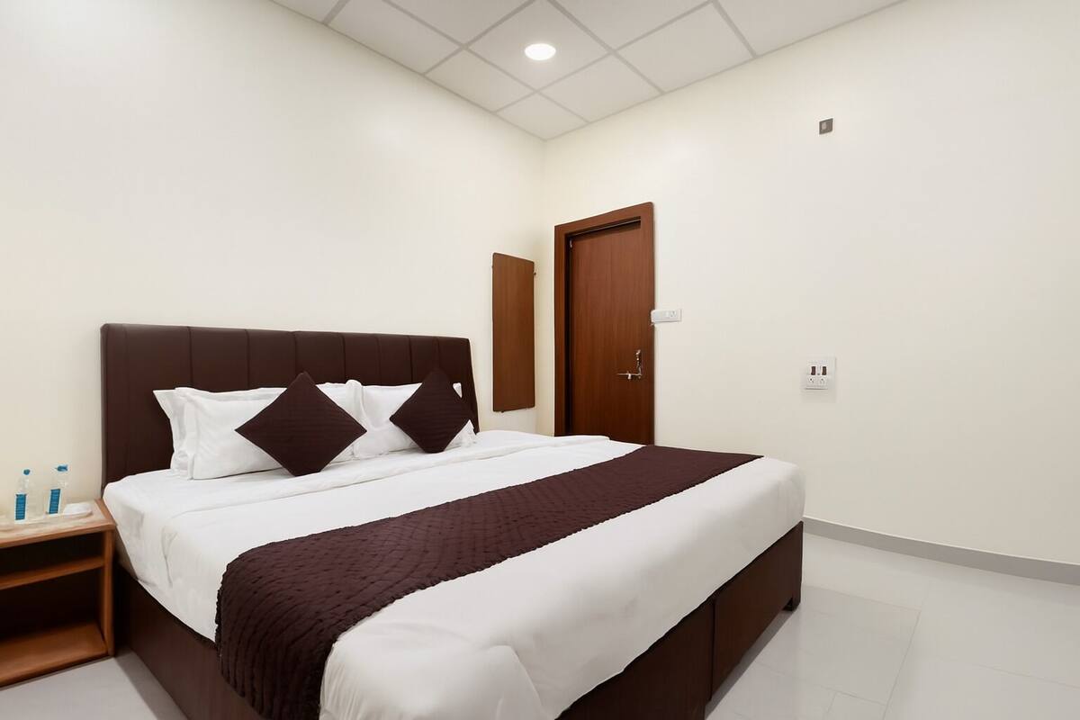Une chambre à coucher bien rangée, avec un grand lit, une tête de lit en bois, une table de chevet avec une lampe et une porte.