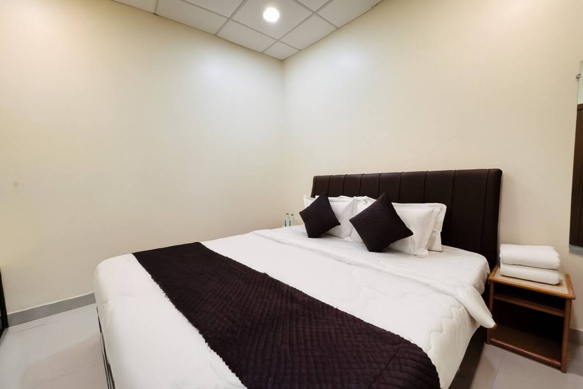 Une chambre d’hôtel avec un grand lit, une table de chevet en bois et un mur blanc.