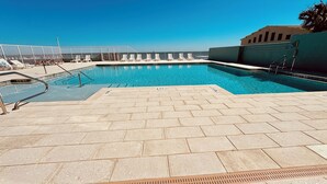 En swimmingpool med kakelbeklädda trappsteg som leder ner i vattnet, omgiven av solstolar och ett staket.