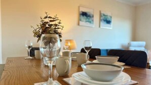 Une table à manger dressée avec de l’assiette blanche, des bols et des verres à vin, et un vase rempli de fleurs séchées placé au centre.