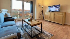 Un salon comprenant un canapé, une table basse, un téléviseur posé sur un meuble et une porte-fenêtre coulissante donnant sur l’extérieur.