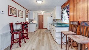 A compact kitchen with wooden cabinets, a central island, and a dining area with two bar stools. - Lake Side Retreat (Inverness)