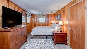 A bedroom with wooden paneling, a bed with a patterned bedspread, a television on a wooden dresser, and a nightstand with a lamp. - Lake Side Retreat (Inverness)