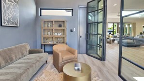 A modern living room with a sofa, armchair, and round coffee table, a wooden cabinet with decorative items, and large glass doors leading to another room.