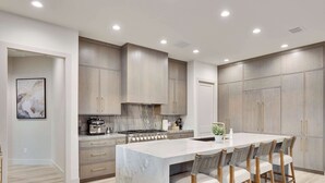 A modern kitchen with marble countertops, wooden cabinets, and bar stools.