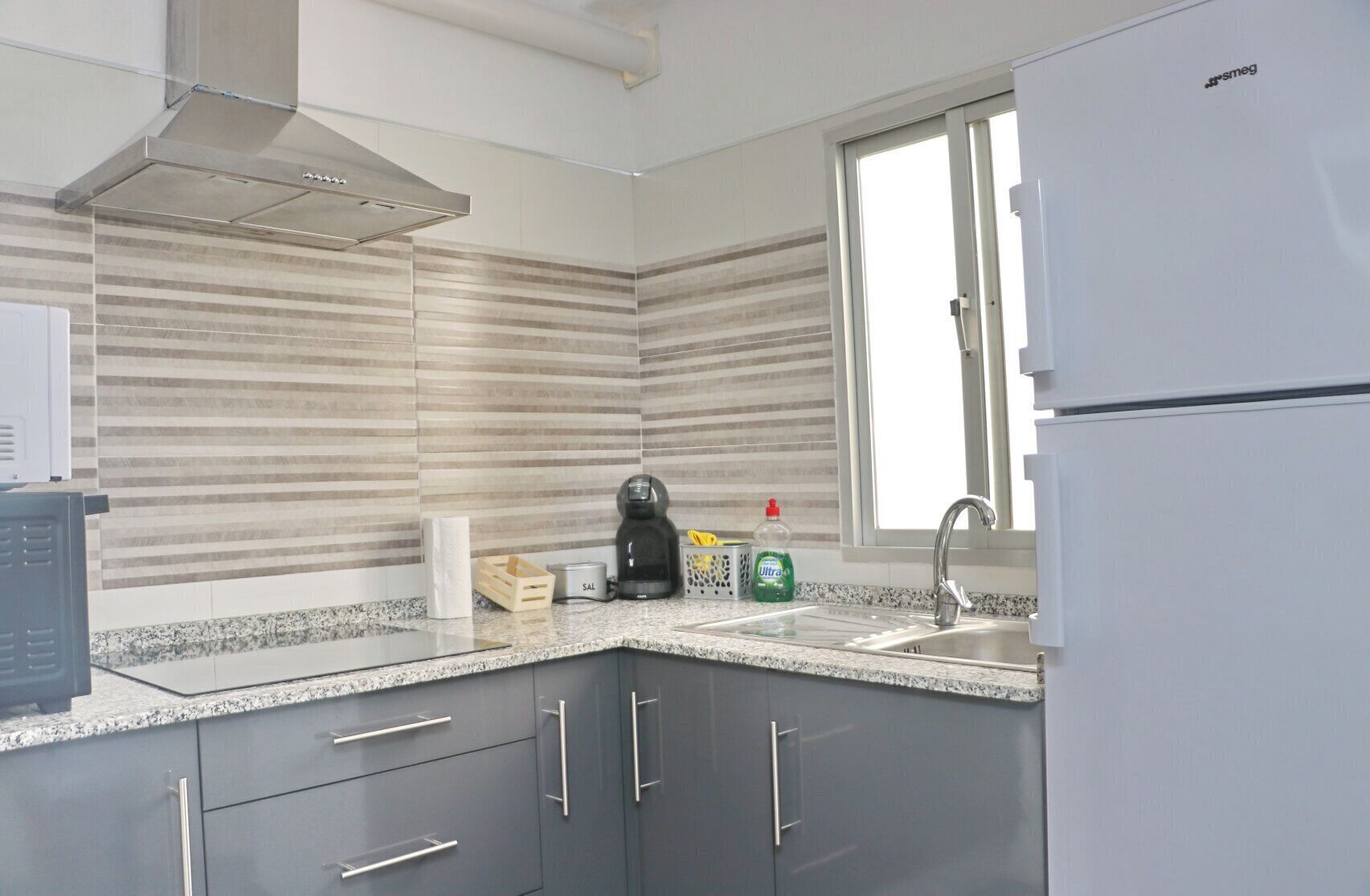 A modern kitchen with a stainless steel range hood, a built-in sink, and a refrigerator.
