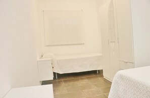A small, clean room with a bed, a nightstand, a wardrobe, and a shower area. - Apartamento Sol y Arena (Conil de la Frontera)