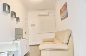 A room with a white desk, a beige sofa, a flat-screen TV, and a painting on the wall. - Apartamento Sol y Arena (Conil de la Frontera)