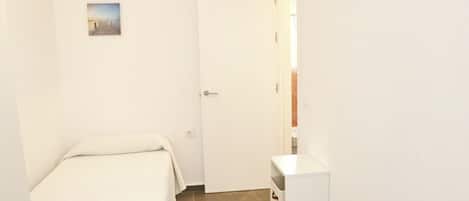 Una habitación pequeña y limpia con una cama, una mesita de noche, una puerta y un cuadro pequeño colgado en la pared.