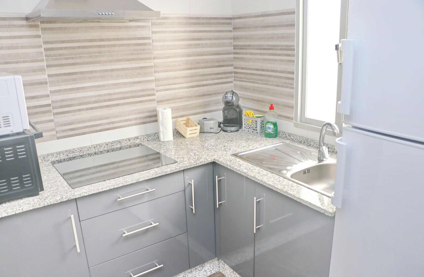 A modern kitchen with granite countertops, a built-in oven, a sink, and grey cabinetry.