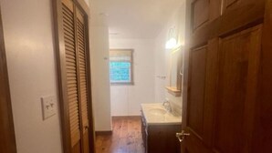 A narrow hallway with wooden doors and a wooden floor leading to a bathroom with a sink and mirror.
