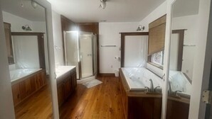 A bathroom with wooden flooring, a bathtub, a sink, and a mirror.