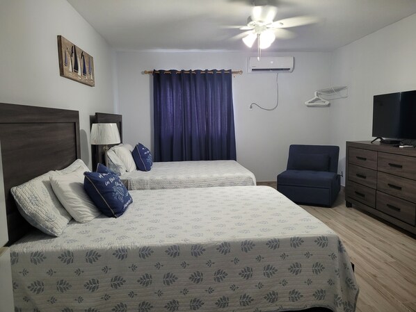 A hotel room with two beds, a ceiling fan, an air conditioning unit, a TV, a chair, and a dresser.