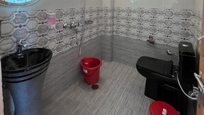 Kylpyhuoneessa on pyöreä peili, musta pesuallas, wc-istuin, punainen ämpäri ja suihkutila.