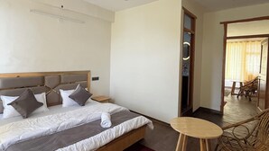 Hotellihuone, jossa on sänky, kattotuuletin, pieni pyöreä pöytä ja punottu tuoli.