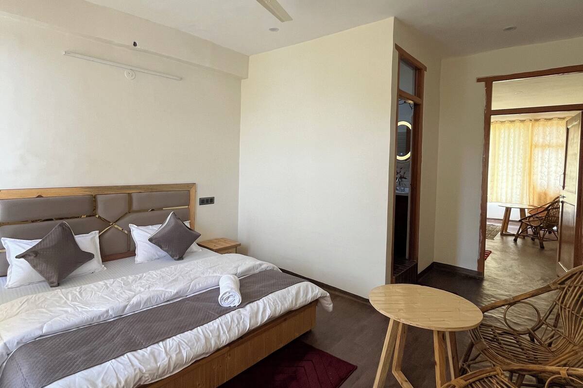 Una habitación de hotel con una cama, un ventilador de techo, una pequeña mesa redonda y una silla de mimbre.