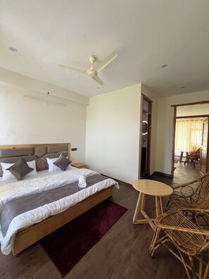 Quarto de hotel com cama, ventoinha no teto, mesa redonda pequena e cadeira de vime.
