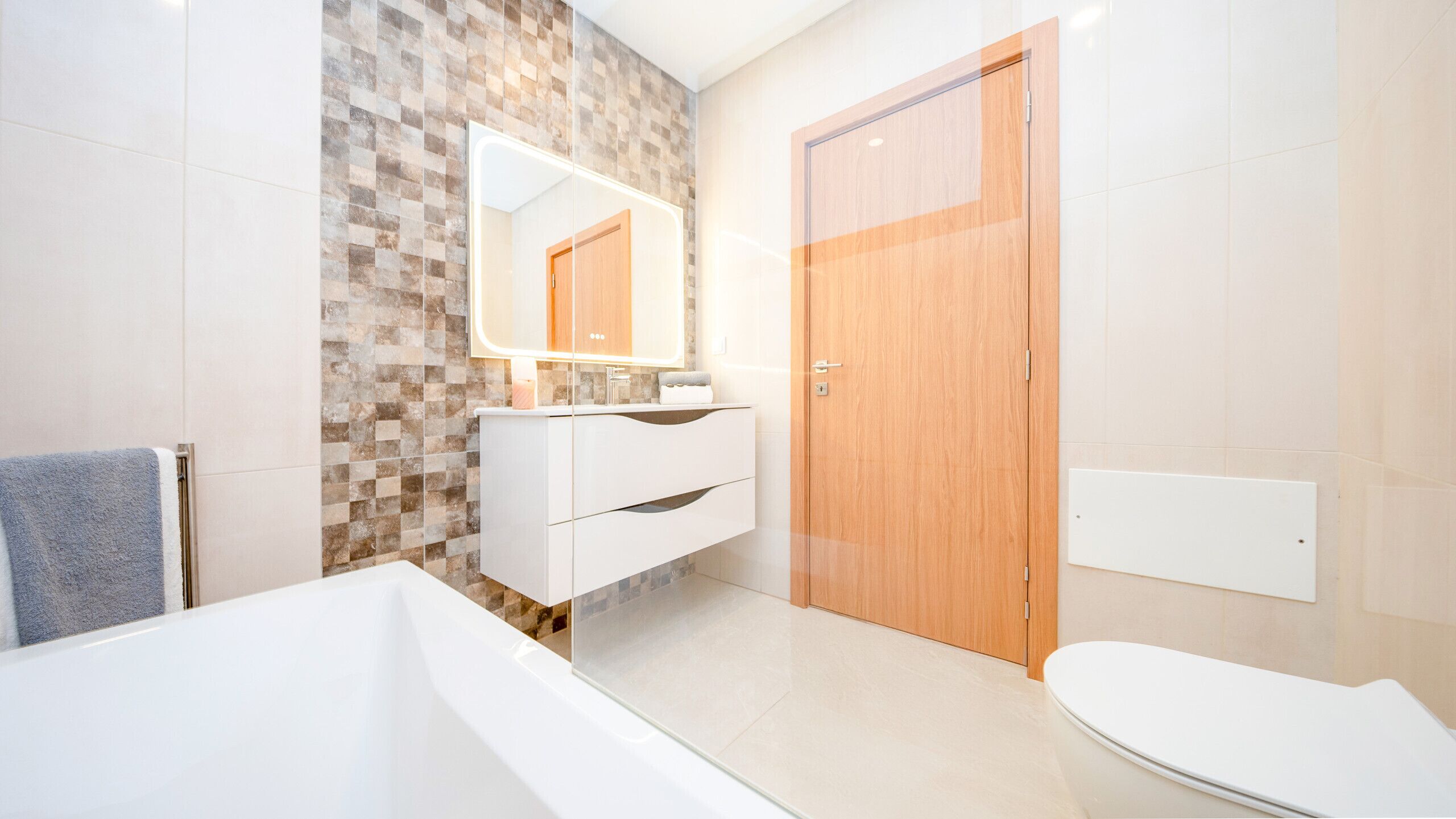 Un baño moderno con bañera, inodoro, tocador con espejo y puerta de madera.