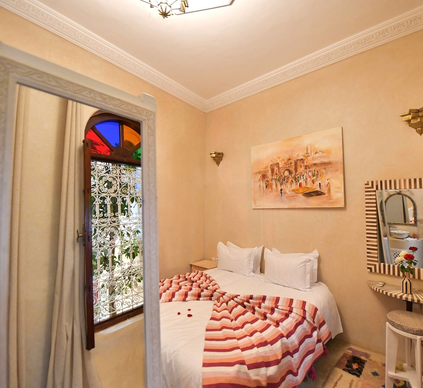 A bedroom with a bed, a painting, a mirror, and a window with a view.