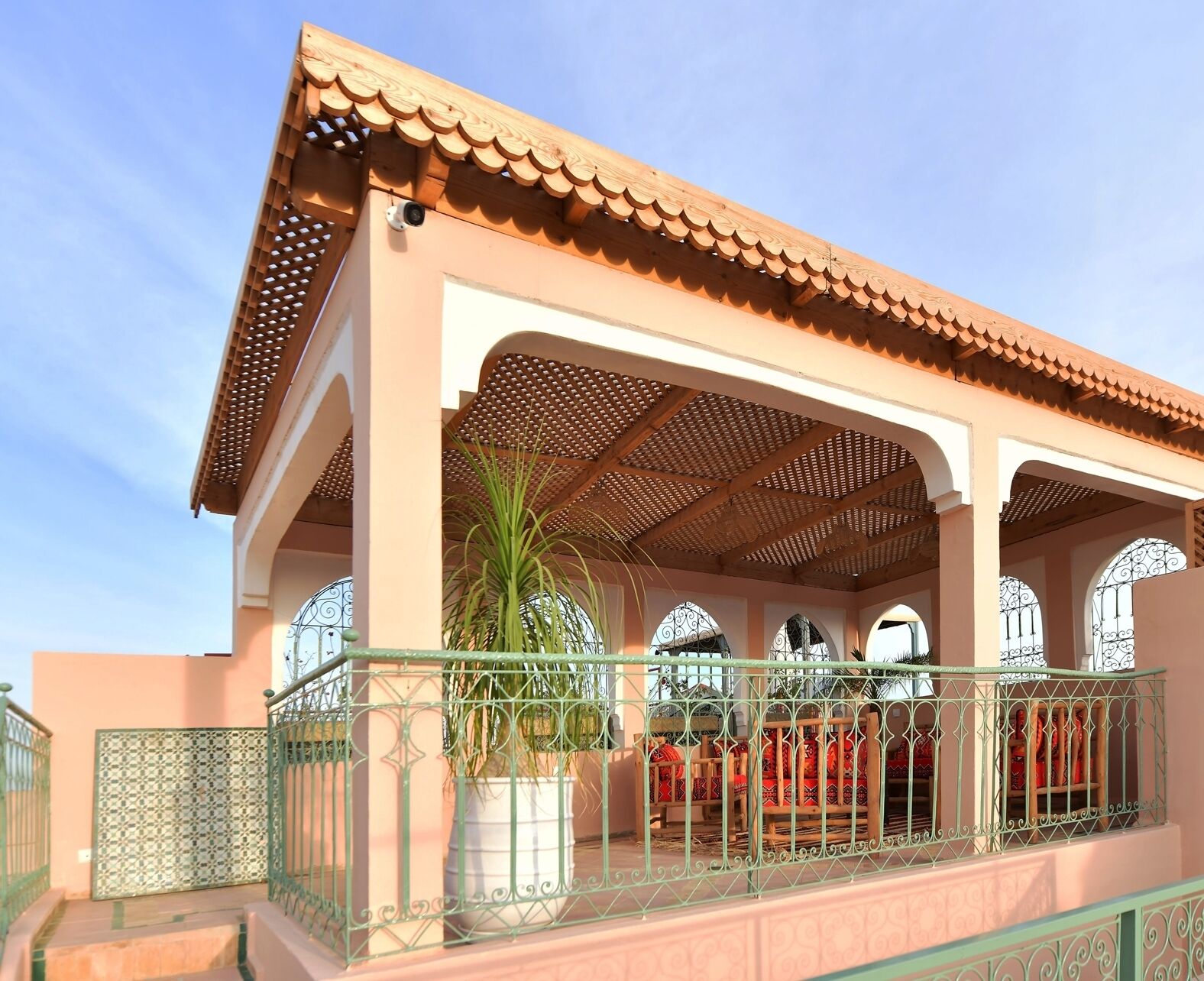 A building with a tiled roof, a covered patio area with a wooden lattice ceiling, and a large potted plant.