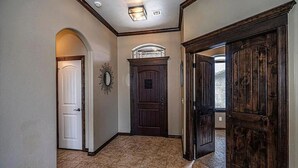 Un pasillo con una puerta blanca, una puerta de madera oscura y un espejo decorativo en la pared.