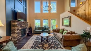A cozy living room with a stone fireplace, two sofas, a coffee table, and a staircase leading to an upper level.