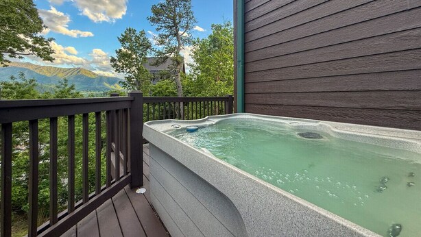 A hot tub on a wooden deck with a view of mountains and trees.