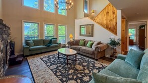 A spacious living room with a stone fireplace, multiple sofas, a coffee table, and a large window overlooking a deck.
