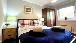 Ein Hotelzimmer mit Bett, Nachttischen, einem Fenster und einem gerahmten Bild an der Wand.