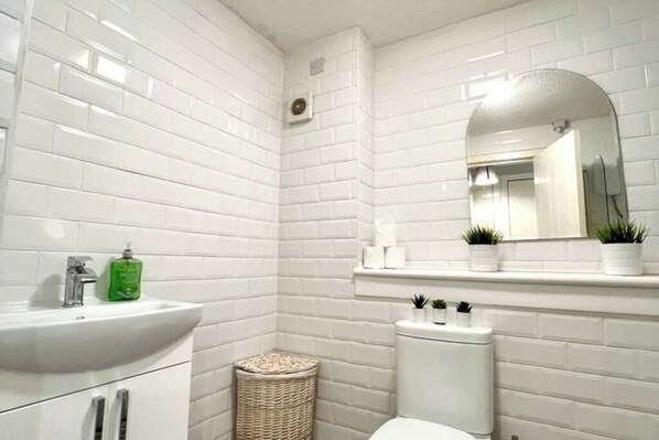 A bathroom with white subway tiles, a white sink, a mirror, and a toilet.