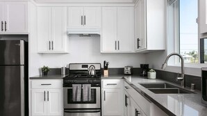 A modern kitchen with white cabinets, stainless steel appliances, and a large window providing natural light. - Urban 3BR Retreat with Modern Amenities (Los Angeles)