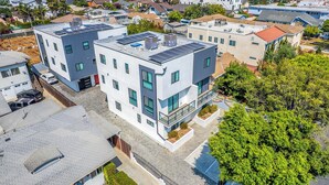 A modern multi-story residential building with solar panels, large windows, and a small rooftop garden. - Urban 3BR Retreat with Modern Amenities (Los Angeles)