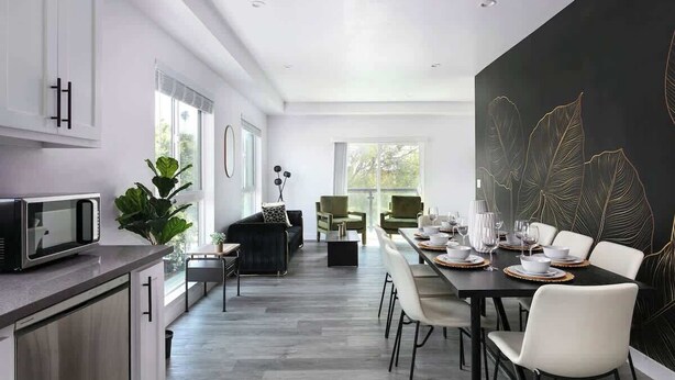 A modern kitchen with a dining area, featuring a large black wall with leaf patterns, a dining table set for six, and a kitchen counter with a microwave. - Urban 3BR Retreat with Modern Amenities (Los Angeles)