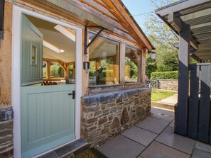 A stone exterior with a green door and windows, a stone wall, and a wooden porch. - 10 Bridge Street (Craven Arms)