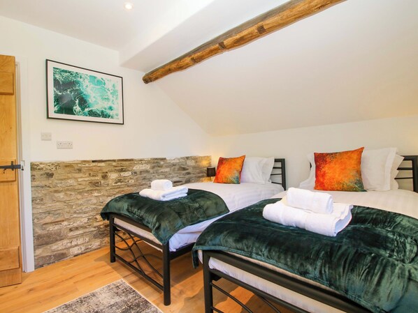 Un dormitorio con dos camas, una pared de piedra, una viga de techo de madera y un cuadro enmarcado en la pared.