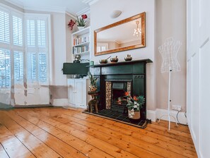A room with a fireplace, wooden flooring, a bookshelf, and a large mirror.