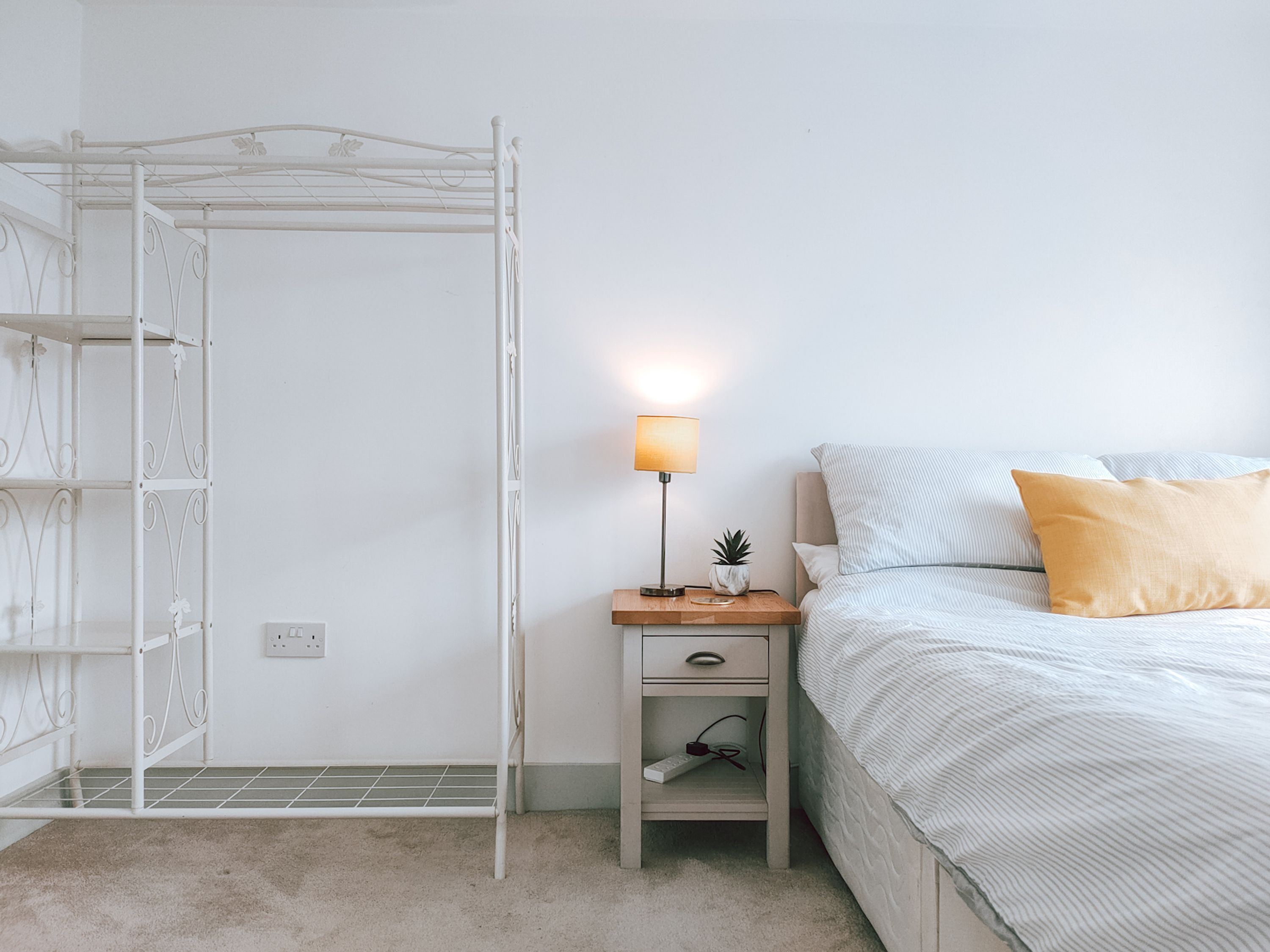 Un dormitorio con cama, mesita de noche, lámpara y armario metálico.