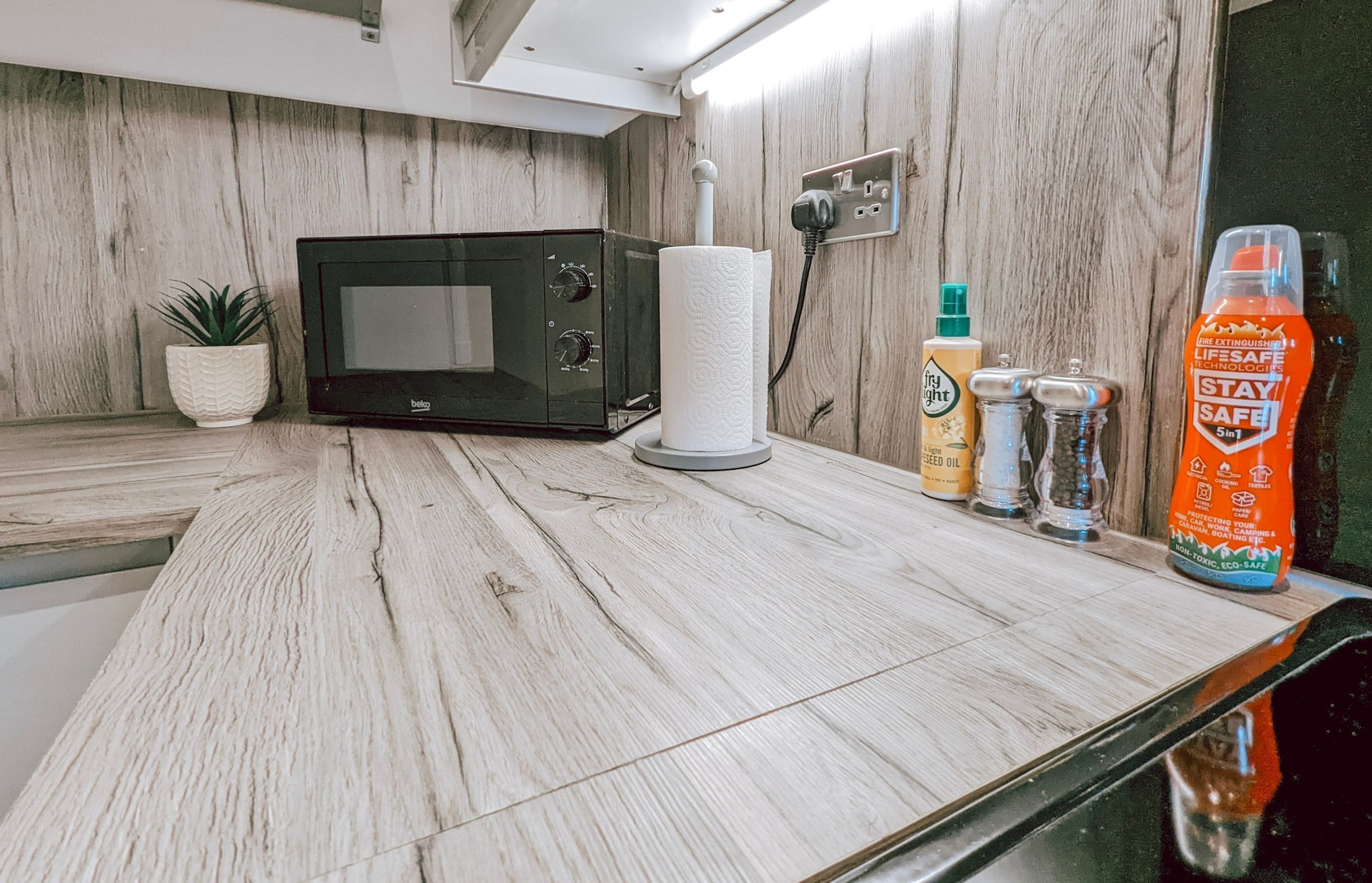 A kitchen with a microwave, a paper towel holder, and a bottle of cleaning product on the counter.