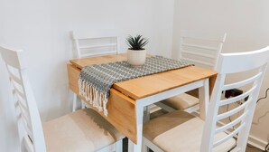 Uma pequena mesa de madeira branca com um jogo americano trançado e uma planta em vaso.