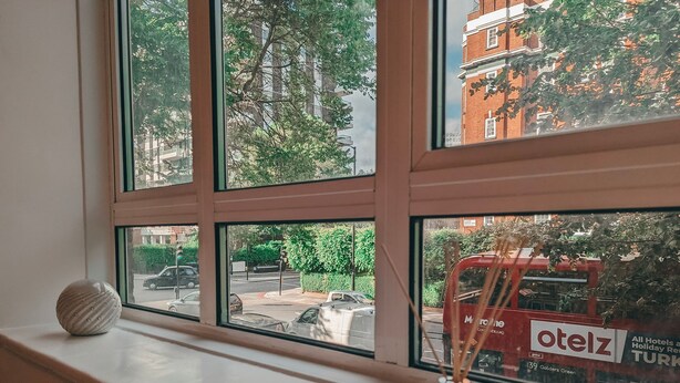 Janela com vista clara para uma rua, um ônibus vermelho e um edifício com o letreiro 'otelz'.