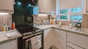 Uma cozinha moderna com fogão preto, armários brancos e janela com vista para o verde.