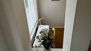 Une pièce avec une fenêtre en arc de cercle peinte en blanc, un bureau avec une lampe et un vase rempli de fleurs.